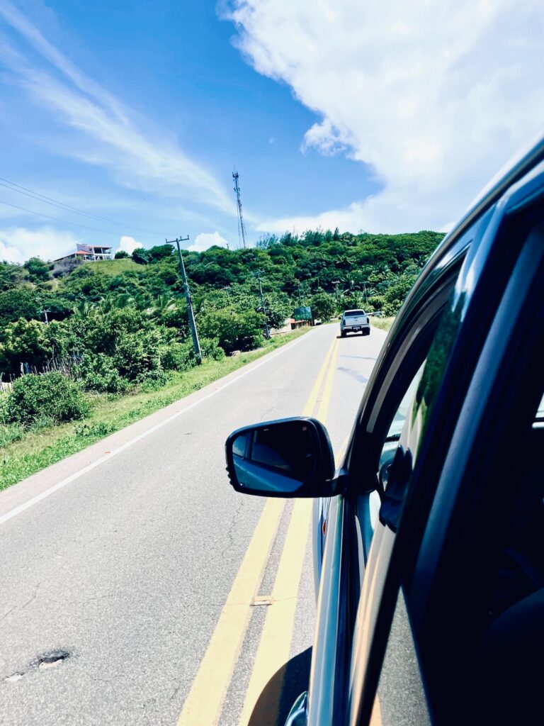 Driving along a coastal road in Ceará state near Fortaleza, with lush green hills and open highway ahead